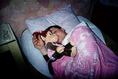 Vintage-style photo of a child sleeping peacefully beside a plush monkey toy, wrapped in a pink floral blanket. The scene evo...