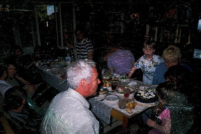 Vintage group dining scene in a dimly lit, festive restaurant. Reflective glass and holiday lights distort reflections. Centr...