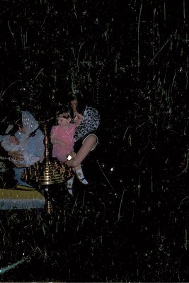 Vintage black-and-white photo of two children playing with a brass candelabra, likely during a fireworks display. The girl in...
