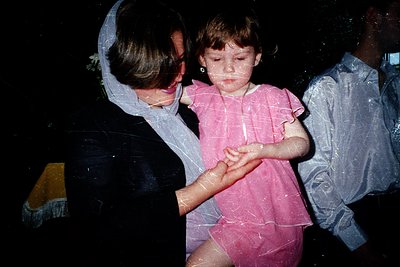 Vintage candid shot of a woman in a white apron and headscarf holding a young girl in a pink dress, both covered in white sub...