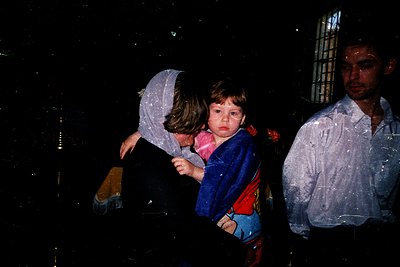 Vintage black-and-white photo of three individuals standing in heavy rain, likely 1970s–1980s. Woman in a hooded coat shields...