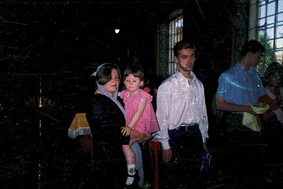 Family portrait in dimly lit indoor setting, likely a 1970s-1980s gathering. Three adults and a child pose on a bench, framed...
