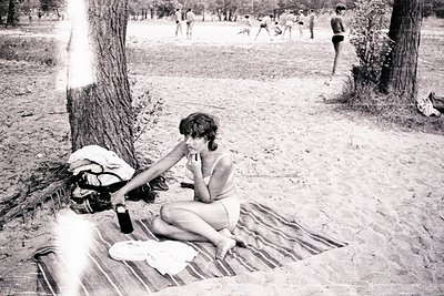 Vintage black-and-white photo of a woman in a bikini sitting on a striped blanket under a tree, holding a bottle. Surrounding...