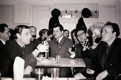 Group of men and women in formal attire, seated around a table with glasses and plates, likely at a 1960s–1970s social gather...