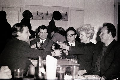 Group of six adults gathered around a table in a formal indoor setting, likely a 1960s–1970s celebration. Men in suits and wo...