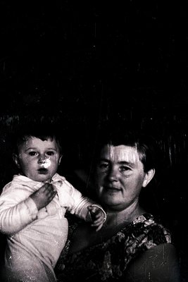 Vintage black-and-white portrait of a woman cradling an infant, likely mid-20th century. The woman’s patterned blouse and inf...