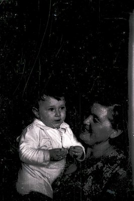 Vintage sepia-toned photo of a young child in a white long-sleeve shirt, seated beside an elderly woman with a blurred, aged ...