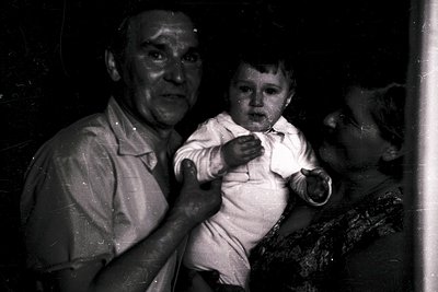 Vintage black-and-white portrait of an elderly man holding a young child indoors, likely mid-20th century. The man’s formal a...