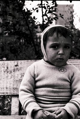 Young child in vintage striped sweater and knitted hat sits on weathered wooden bench, outdoors. Soft focus and sepia tone su...