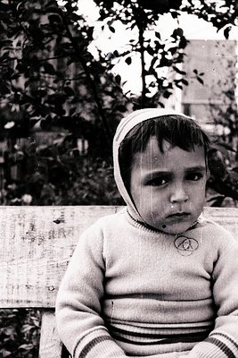 Vintage black-and-white portrait of a young child wearing a striped sweater and knitted cap, seated on a wooden bench. The ch...