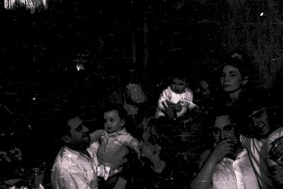 Vintage black-and-white photo of a family group portrait in dim lighting, likely mid-20th century. Three adults and two child...