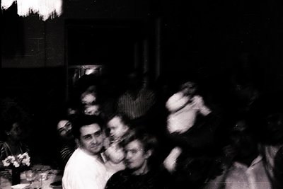 Vintage black-and-white photo of a lively indoor gathering, likely a 1960s–1970s party. Blurred motion captures dynamic danci...