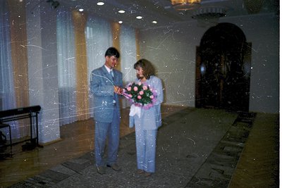 Couple holding bouquet of pink roses in grand hall with marble floors and arched doorway, 1970s-80s Eastern Bloc style. Forma...