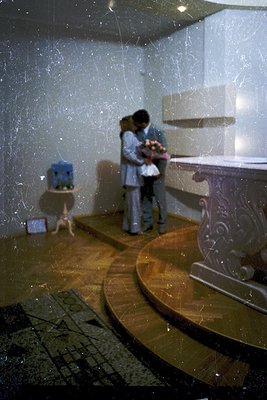 Vintage indoor shot of a couple embracing near a curved marble countertop, likely a kitchen or bathroom. The scene includes a...