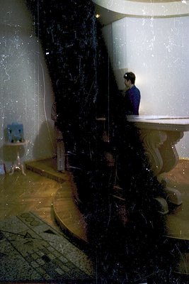 Vintage-style bathroom with ornate black marble column and curved sink. A person in a dark jacket and cap stands near a vinta...