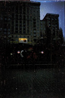 Vintage urban night scene featuring a multi-story, Art Deco-style building with illuminated balconies and a billboard adverti...
