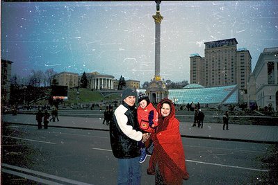 Family portrait in Independence Square (Maidan Nezalezhnosti), Kyiv, Ukraine, 1990s. Three individuals pose in winter attire—...