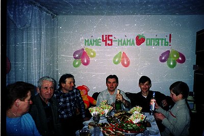 Family celebration for a 45th birthday ("мама опять!" = "mom again!") in a dimly lit indoor setting, likely Eastern Europe, 1...