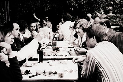 Group dining outdoors in 1970s Eastern Europe, likely Bulgaria. Long table laden with plates, glasses, and food—likely a comm...