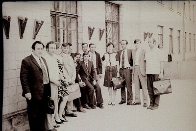 Group portrait of 12 individuals in formal attire, likely 1960s–1970s Eastern Bloc. Men in suits, ties, and briefcases; women...