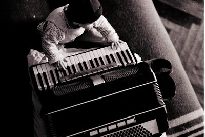 Vintage accordion with rolled-up strap, played by hands in a close-up shot. Mid-20th century design suggests portable, portab...