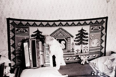 Vintage black-and-white photo of a child standing beside a decorative wall-hanging featuring geometric and nature motifs (pin...