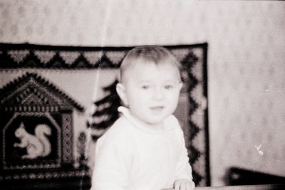 Vintage black-and-white portrait of a young child indoors, wearing a collared shirt. Decorative wall tapestry with geometric ...