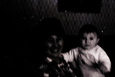 Vintage black-and-white photo of two infants in close proximity, likely mid-20th century. The child on the right wears a shor...