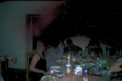 Vintage-style party scene with long-exposure light trails creating dynamic motion blur. Indoor setting featuring a long table...