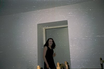 Vintage candid shot of a woman in a sleek black dress posing in a dimly lit doorway, framed by textured concrete walls. Refle...