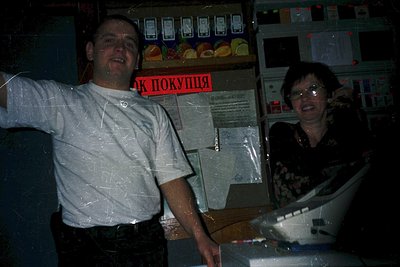 Vintage photo of two individuals posing in a Soviet-era grocery store, likely late 20th century. Man in white shirt gestures ...