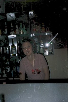 Barback in a modern cocktail lounge, holding two martini glasses with decorative straws. Glass shelves behind display an arra...