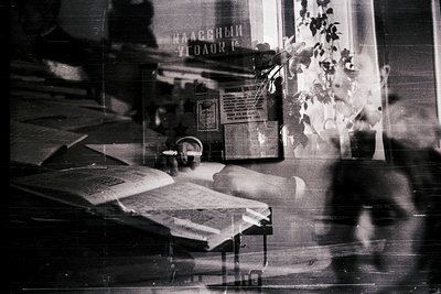 Vintage black-and-white shot of a cluttered study desk with Cyrillic signage ("Научный Вклад" visible). Stacked books, papers...