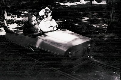 Mid-20th century black-and-white photo of children riding a wooden roller coaster car, likely from a vintage amusement park. ...
