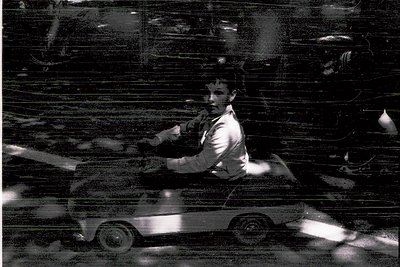Black-and-white street scene featuring a man in a suit riding a vintage motorcycle, blurred motion emphasizing speed. Reflect...