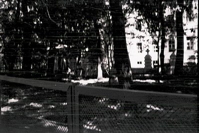 Vintage black-and-white reflection in a windowpane showing a courtyard with brick walls, a statue, and trees. Distorted but r...
