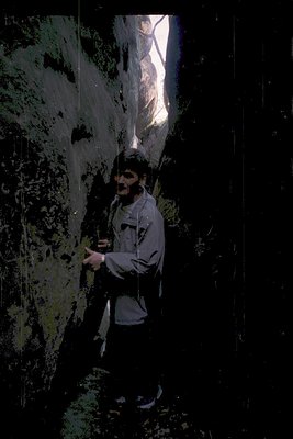 Climber ascending a narrow, vertical rock face in low-light conditions, gripping a rope secured overhead. The rugged terrain ...