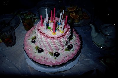 Decorated birthday cake designed as a smiling face with fondant details, featuring 12 lit candles. The message "Happy Birthda...