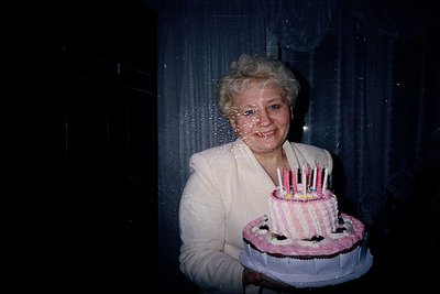 Vintage birthday portrait featuring a woman holding a tiered pink/white cake with lit candles. Soft focus and warm lighting e...