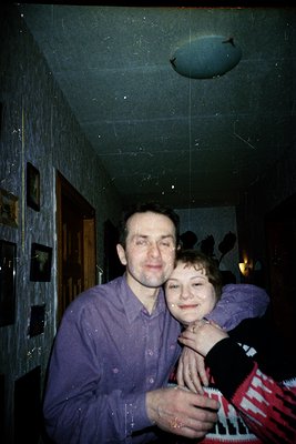 Vintage indoor portrait of a man and child in a dimly lit room, likely 1970s–1980s. The man wears a button-down shirt, and th...