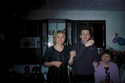 Vintage indoor portrait featuring three adults in a dimly lit room with frosted glass walls. The man holds a glass of champag...