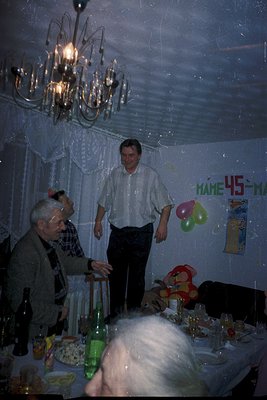 Vintage indoor celebration with three men in 1970s attire—one in a white shirt, another in a checkered shirt, and a third in ...