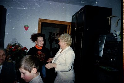 Vintage indoor gathering featuring a woman in a white blazer and a young girl in a graphic sweater, likely 1980s-1990s. Decor...