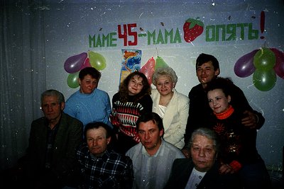 Family celebration for a 45th birthday, likely Eastern Europe, 1980s–1990s. Indoor setting with hand-painted banner reading "...