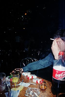 A person rests their head on a table in a dimly lit, festive setting, with hands covering their face. The table displays a ha...