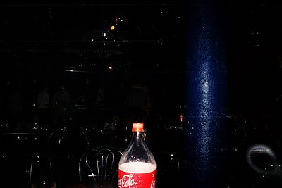 Vintage Coca-Cola bottle in dimly lit, foggy indoor setting. Classic glass bottle with iconic red label, likely mid-20th cent...