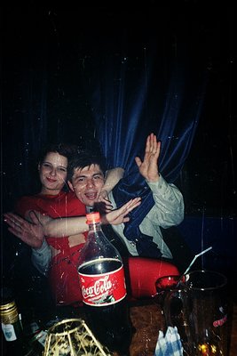 Vintage party scene with two joyful individuals clapping, framed by a curtain of confetti. A red Coca-Cola bucket and empty b...