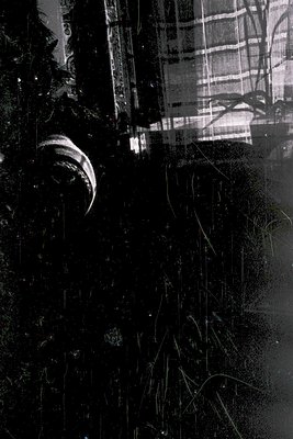 Vintage black-and-white photo of a **pleated curtain** with visible wear, framing a **window sill** and **street scene** belo...
