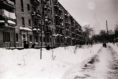 Mid-century Soviet-era apartment block row in snow, featuring uniform brick facades with small balconies. Pedestrians in wint...