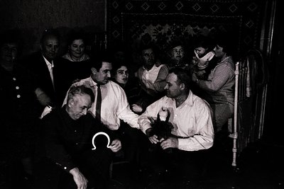 Vintage black-and-white photo of a formal indoor gathering, likely a 1920s–1930s European event. A seated man in a white shir...